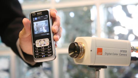 Contents from a surveillance camera are being fed into the mobile phone via a computer through streaming technology.	